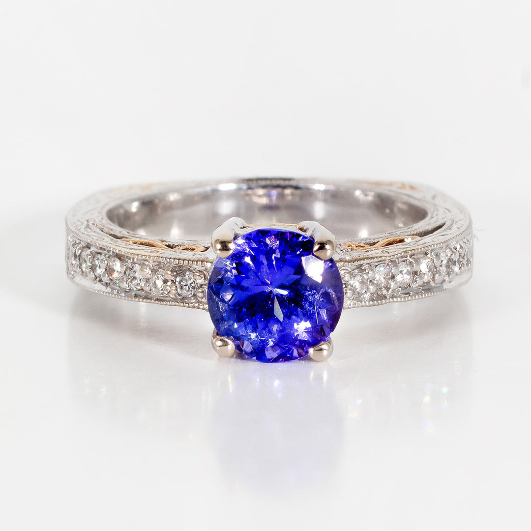 Square shank ring in 18K two-tone with engravings all around the shank, pave set round diamonds, and 4-prong set tanzanite center stone. D0.14ct.t.w. Tanzanite 1.35ct.