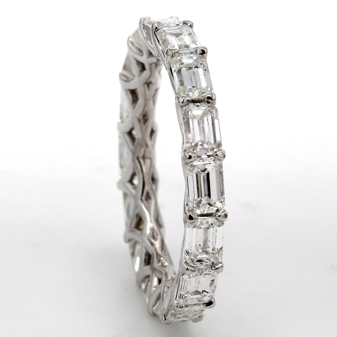 East to west style eternity band in 18K WG with shared U-prong set (16) emerald cut diamonds. D3.86ct.t.w. Size 6.75