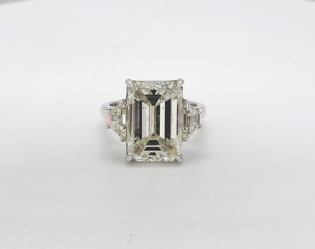 3-stone ring in platinum with GIA certified L/SI2 emerald cut center and basket prong set trapezoid diamond side stones. D10.50ct.t.w. (Center - 9.17ct.) Size 6.75