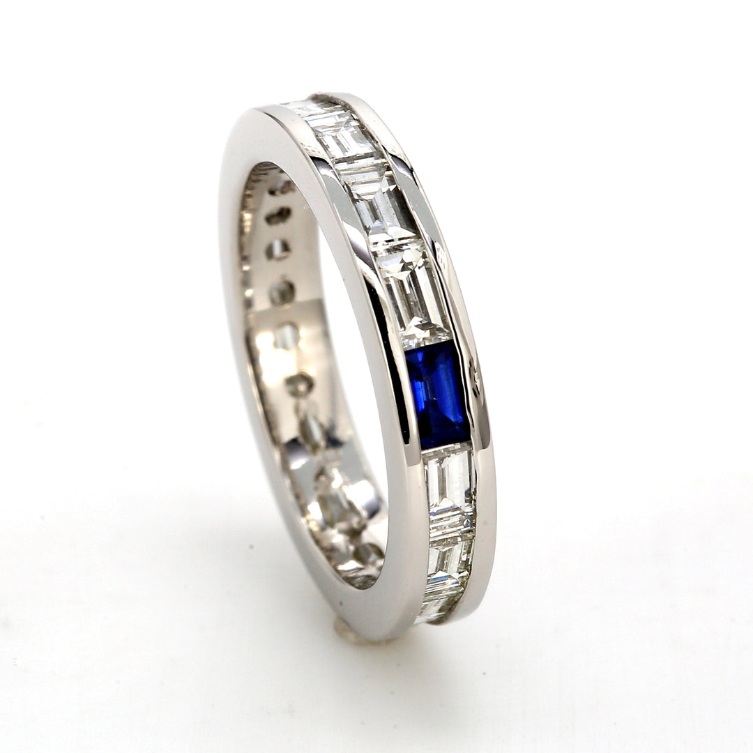 Eternity band in platinum with channel set baguette diamonds &  a baguette shaped sapphire.  D1.38ct.t.w.  Sapphire 0.12ct.