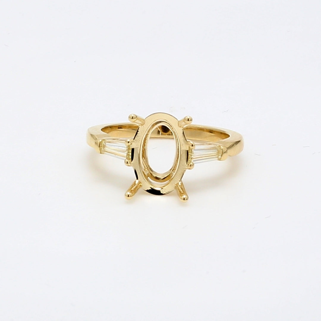 Three stone semi-mount in yellow gold for oval center size with tapered bagutte diamond sides.  D0.38ct.t.w.  Size 6